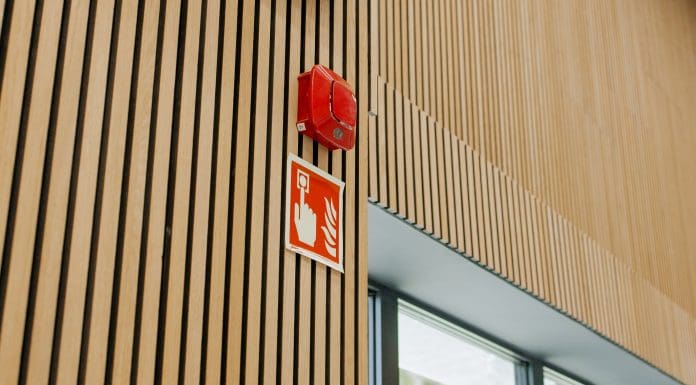 Red fire alarm and fire emergency sign on a modern wooden slat wall inside a public building, close-up safety equipment, representing Code for Construction Product Information