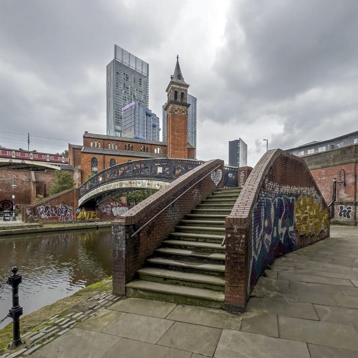 View across the canal at Castlefield in the centre of Manchester, UK. Reflections of a foot bridge and graffiti can be seen. There are no people in the photograph