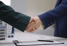 Martin Staehr to lead Kier Construction business Two professionals shake hands over architectural blueprint plans with a contract successful agreement or business partnership in a corporate business with architectural models, representing the appointment of Martin Staehr