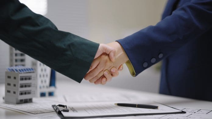 Two professionals shake hands over architectural blueprint plans with a contract successful agreement or business partnership in a corporate business with architectural models, representing the appointment of Martin Staehr