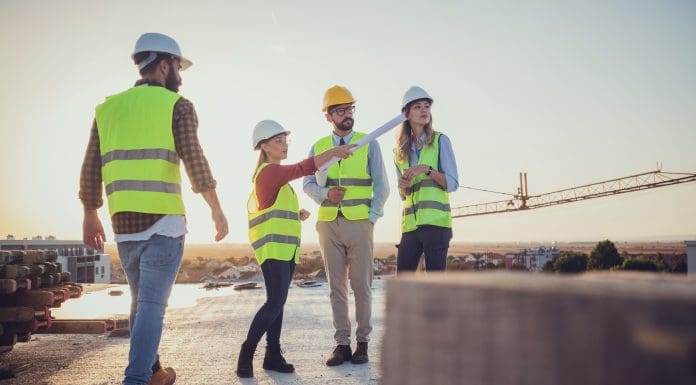 omparing with the blueprints, a team of experts is evaluating the realization on the construction site. For their own safety, all members have yellow vests and hard hats.