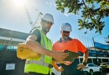 Project Management Day: Deltek’s Bret Tushaus reflects on the ‘unsung heroes’ of the industry Two engineers wearing hardhats and high-visibility vests are discussing building plans at a construction site in australia, representing Project Management Day