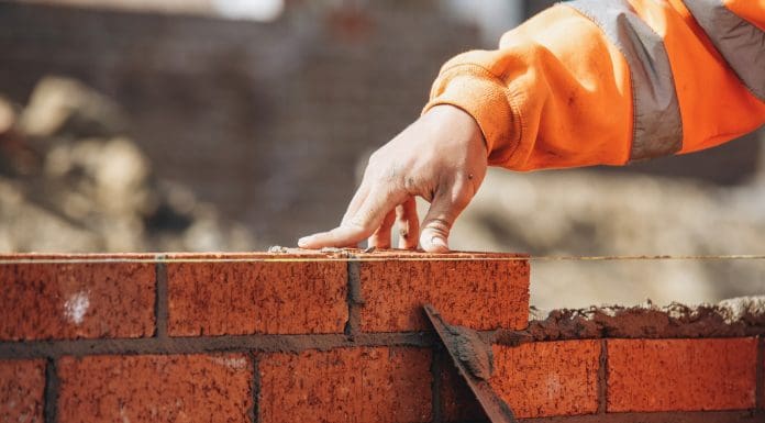 Bricklayer laying another brick in the wall on construction site for sturdy wall