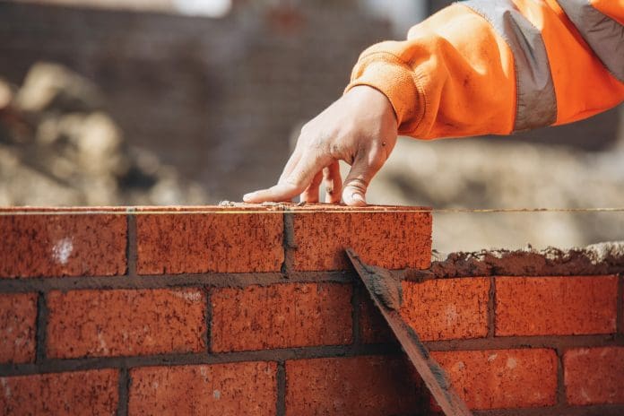Bricklayer laying another brick in the wall on construction site for sturdy wall