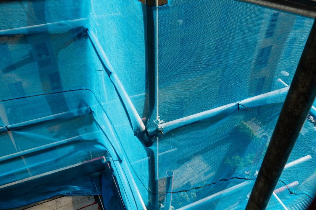 View of the exterior of a high-rise building that is having work done on its exterior. There is scaffolding set up around the building with safety nets for safety.