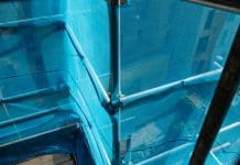 Lords Committee deems Building Safety Regulator delays “unacceptable” View of the exterior of a high-rise building that is having work done on its exterior. There is scaffolding set up around the building with safety nets for safety.