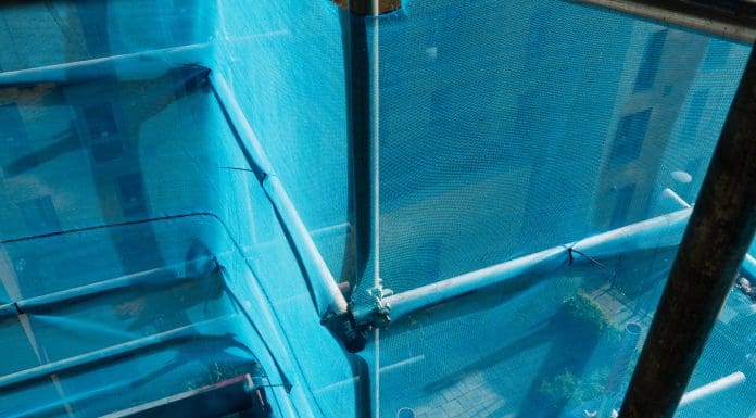 View of the exterior of a high-rise building that is having work done on its exterior. There is scaffolding set up around the building with safety nets for safety.