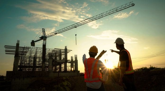 Silhouette of team engineer using laptop to control work, crane, construction site.