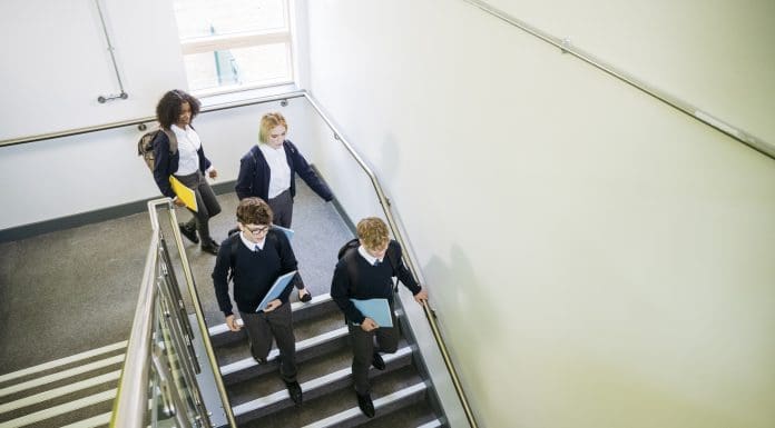High angle view of British teenagers in uniforms carrying backpacks and notebooks as they move down steps in education building, representing Free schools building programme cuts