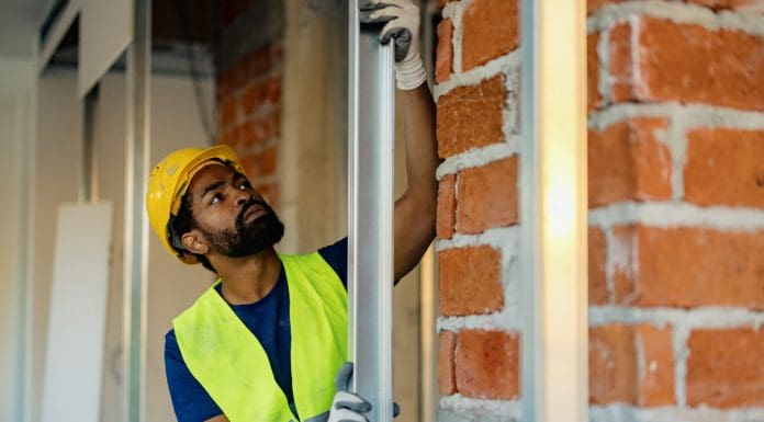 Worker in protective gear and safety vest inspecting a metal frame during construction. Bright lighting highlights tools, showcasing work in progress for a building interior concept, representing material passports