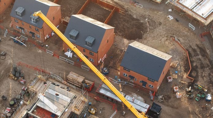 Aerial view of yellow mobile crane lifting materials on construction site, representing the new Single Construction Regulator prospectus