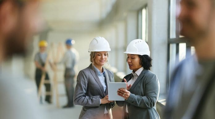 Female real estate developers cooperating while surfing the Internet on digital tablet at construction site, representing construction email management