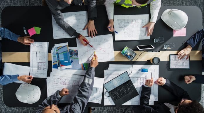 Top Down View of Diverse Team of Business Professionals and Engineers Working Together on Architectural Plans in a Corporate Office. Focused Colleagues Using Laptop, Tablet, Blueprints and Documents.