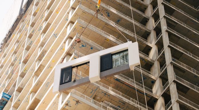 Installing a piece of a modular facade on a building under construction, representing the role offsite manufacturing could play in social housing