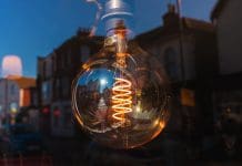 CIBSE conference sets benchmark for future building performance Edison light bulb with visible filament hanging in a window, reflecting a city street view at dusk, representing building performance
