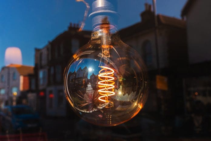 CIBSE conference sets benchmark for future building performance Edison light bulb with visible filament hanging in a window, reflecting a city street view at dusk, representing building performance