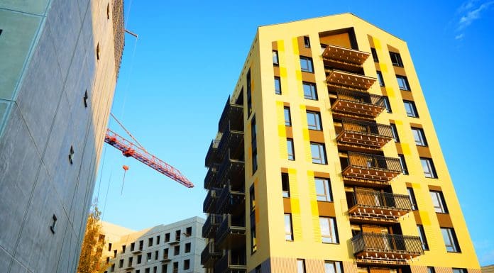 Building under construction. Facade of residential building in bright yellow paint. Modern Architecture. Cranes on building construction. New built modern house, renovation. Condo complex construction