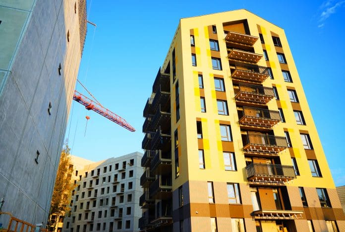 Building under construction. Facade of residential building in bright yellow paint. Modern Architecture. Cranes on building construction. New built modern house, renovation. Condo complex construction