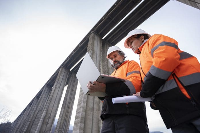 Team of experienced road engineers in safety gear and helmets discuss new viaduct blueprint of highway construction project. Building smart infrastructures. Representing SCIA Engineer 2026