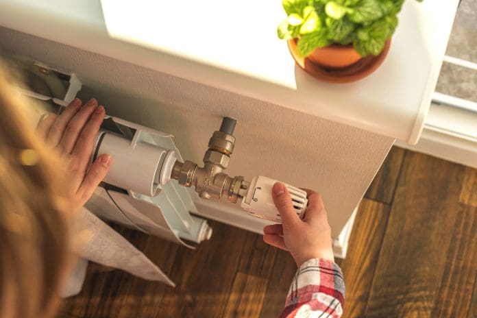 Woman adjusting the temperature on valve of a radiator at home, modern interior background photo How to best deliver the Warm Homes Plan – that’s the £15bn question