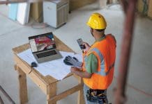 Who owns your project data? The question CIOs can no longer avoid A worker in hi viz and yellow hard hat checking a phone. They are stood in front of a table covered with blueprints and a laptop