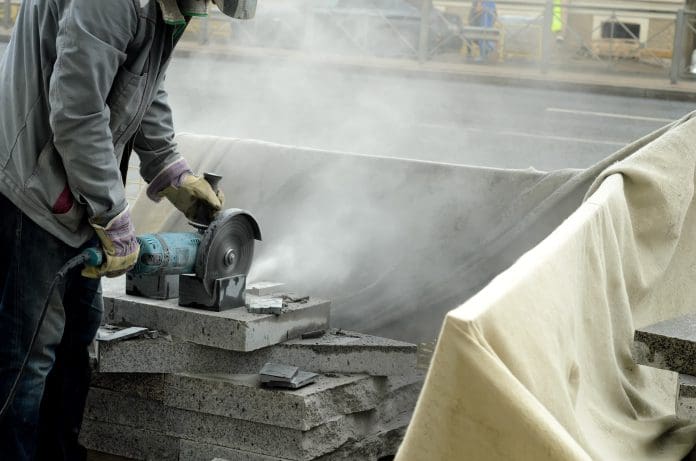 The worker cuts a big powerful angle grinder paving slabs. Failure to comply with engineered stone bans could lead to site shutdown, FMB warns