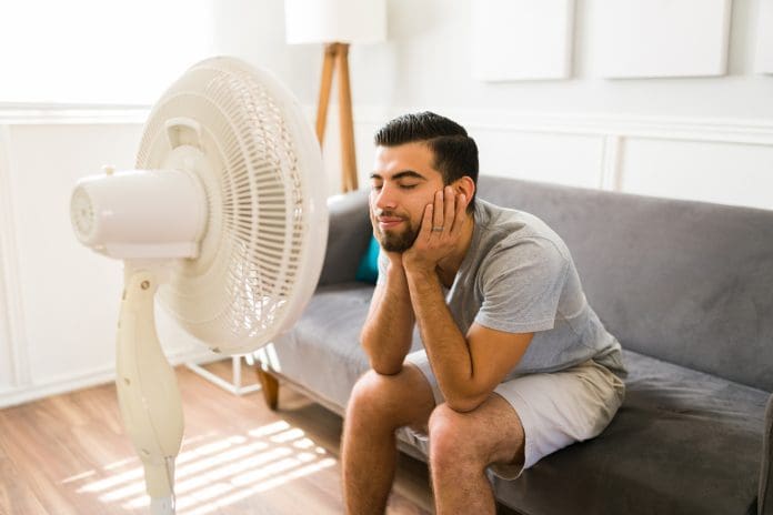 Relieved man enjoying the electric fan UK buildings in heatwaves can become insufferable places