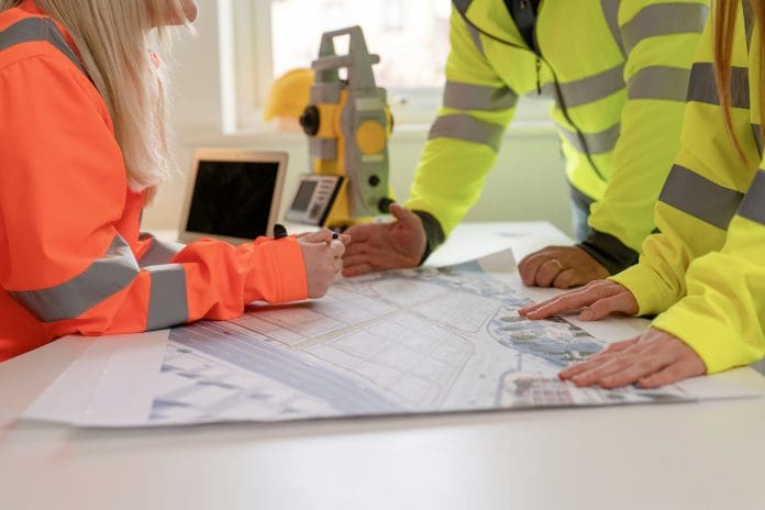 Engineering professionals collaborate on construction plans in bright office wearing safety hi-viz gear Slow decision-making could cost construction firms £1.1bn a year