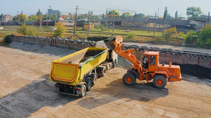 Loader filling yellow tipper truck with gravel at industrial site A HS2 contractor was injured by a falling tipping truck and the responsible JV was fined £400,000