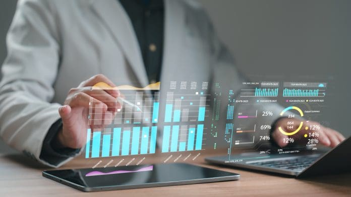 Business person analyzes financial data using digital tablet and laptop, interacting with futuristic holographic interface displaying charts, graphs, and market statistics in modern corporate office. How AI and automation are changing financial planning in construction
