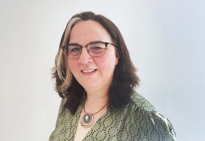 A picture of Georgina Mullen standing against a light grey background smiling towards the camera