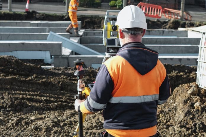 Construction worker stands focused on surveying equipment at a construction site. The worker wears safety gear and oversees groundwork for a new building The CECA say that updated RIDDOR regulations must be clearer for civil engineers