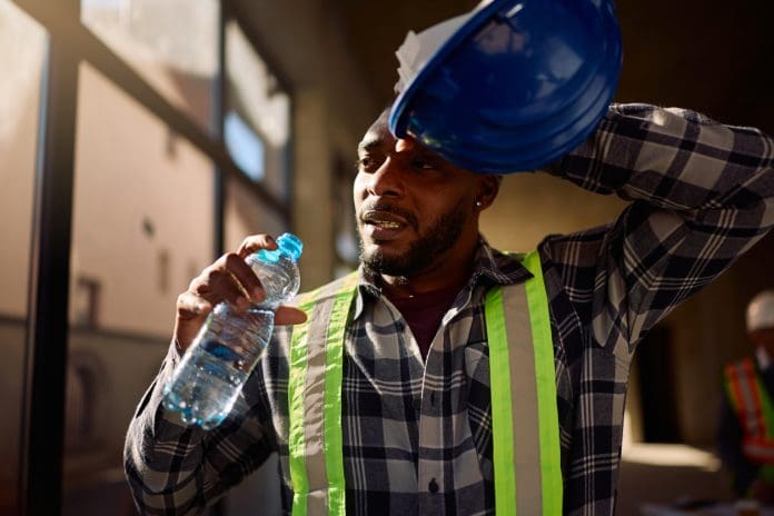 Exhausted black worker drinking water at construction site. African American construction worker refreshing himself with a water at work.