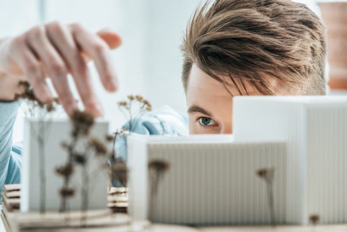 partial view of young architect looking at self made building model in office partial view of young architect looking at self made building model in office