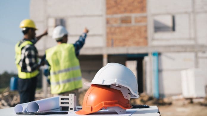 Structural engineer and architect working with blueprints discuss at the outdoors construction site. UK construction decline slows for the first time in four months