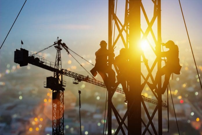 Silhouette of Engineer and worker working crane on steel structures industrial project at building site background, construction site at sunset in evening. Infrastructure, High-rise building Industry Construction has changed – but there is more to do