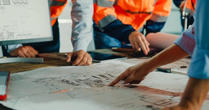 Closeup of team of industrial engineers meeting analyze machinery blueprints consult project on table in manufacturing factory. Working in manufacturing plant or production plant. Closeup of team of industrial engineers meeting analyze machinery blueprints consult project on table in manufacturing factory. Working in manufacturing plant or production plant concept.