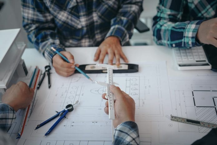 Team of engineers in a meeting, drawing blueprints for condo, apartment, and house construction. Negotiating costs with contractors, bidding, bargaining, and cooperating on construction sites. Construction bid teams must face an increasingly complex series of hurdles