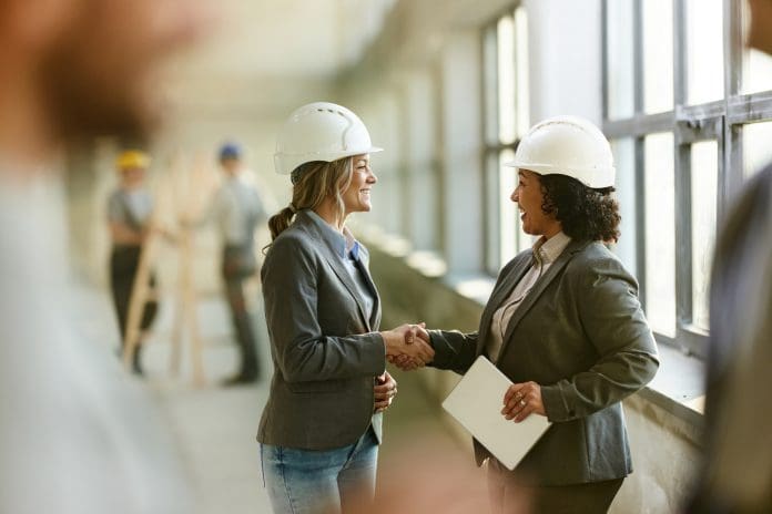 Happy female building contractors shaking hands at rebuilding site. Procurement opens for £8bn national construction framework