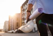 Council housebuilding set for major revival under £39bn programme Unrecognisable engineer, architect or worker holds in hand protective white hard hat and blueprint on multi-apartment residential complex background, sunlighting. Concept of new real estate
