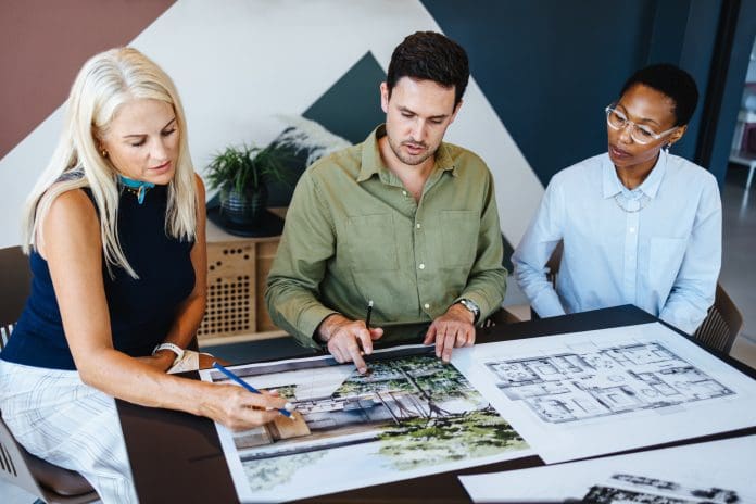 Group of diverse professionals discussing architectural blueprints in a modern office setting The ARB Prescribed Examination offers a pathway for non-UK architects to join the register
