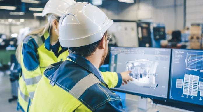 Two workers in hard hats and high visibility jackets looking at a computer monitor displaying a digital model of a building project