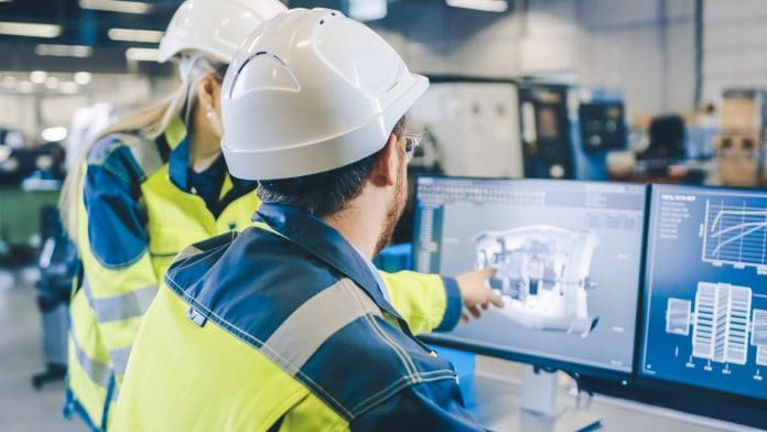 Two workers in hard hats and high visibility jackets looking at a computer monitor displaying a digital model of a building project