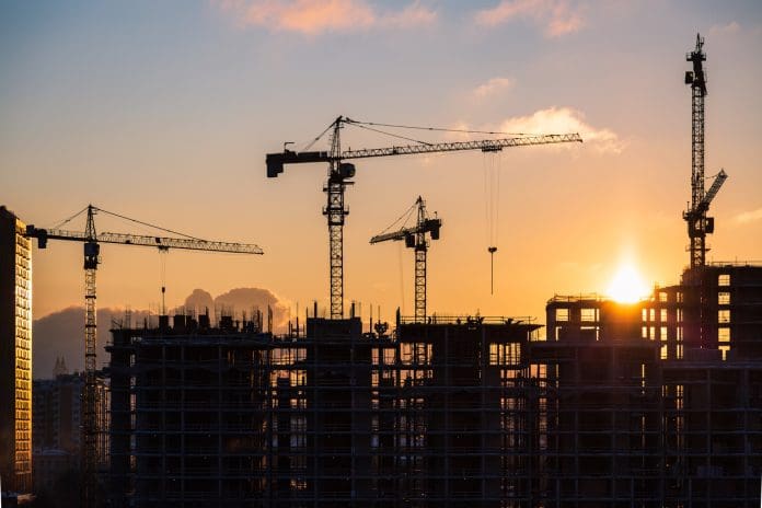 Building site at sunset Lots of tower cranes build high-rise residential building in evening time. Steel frame structure in sunlight. Industrial background with sun flare. Yellow sunset sky.