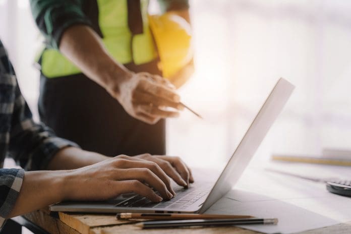 business man hand working and laptop with on on architectural project at construction site at desk in office. business man hand working and laptop with on on architectural project at construction site at desk in office.