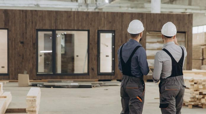 Two engineers are evaluating a finished prefabricated modular building inside a large factory, ensuring quality and compliance