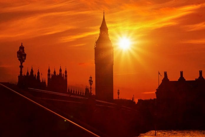 Big Ben heatwave sunset with intense sunlight - London, UK The intense summer sun blazes over London, casting a fiery glow on Big Ben and the Houses of Parliament. The sky is drenched in deep orange and red hues, evoking the scorching heat of a heatwave. The shimmering light creates a dramatic and almost surreal atmosphere, emphasizing the extreme weather conditions.