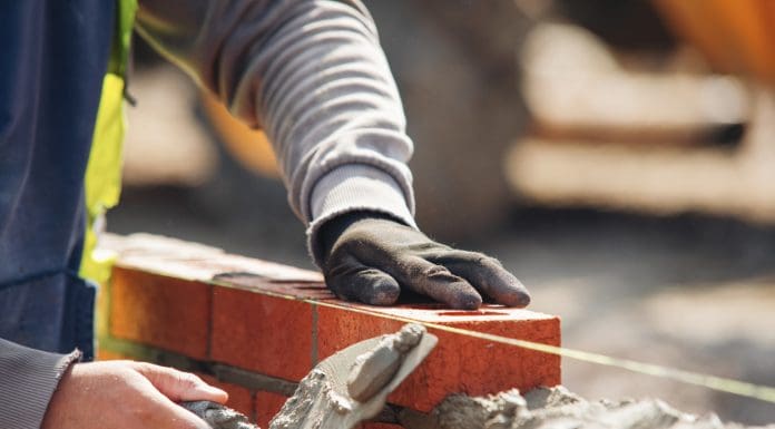 Bricklayer constructing stone wall using bricks, cement mortar mix and trowel