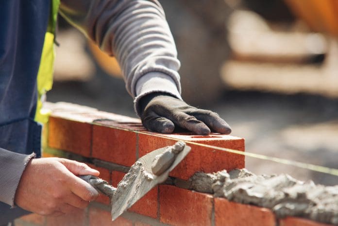Bricklayer constructing stone wall using bricks, cement mortar mix and trowel Bricklayer constructing stone wall using bricks, cement mortar mix and trowel