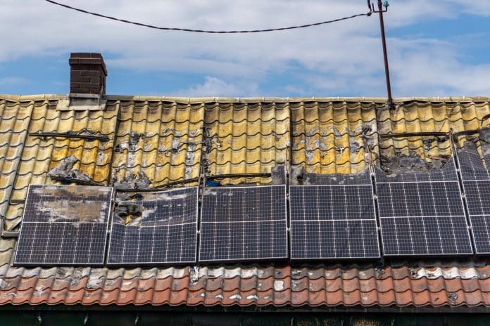 Burnt building roof after fire – damaged solar panels and scorched roof tiles with visible fire damage. Solar panel fires can be avoided using linear heat detection